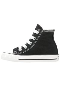 Sorte kanvas høyhælte sneakers med hvite snøringer, gummitåhette og kontrastsøm. Hvit såle med svart stripe langs bunnen.