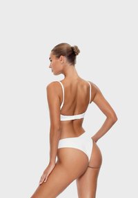Witte bikini met een eenvoudig ontwerp, smalle bandjes en een haaksluiting op de rug. Soepele stof, minimale bedekking en een hoge beenuitsnijding.