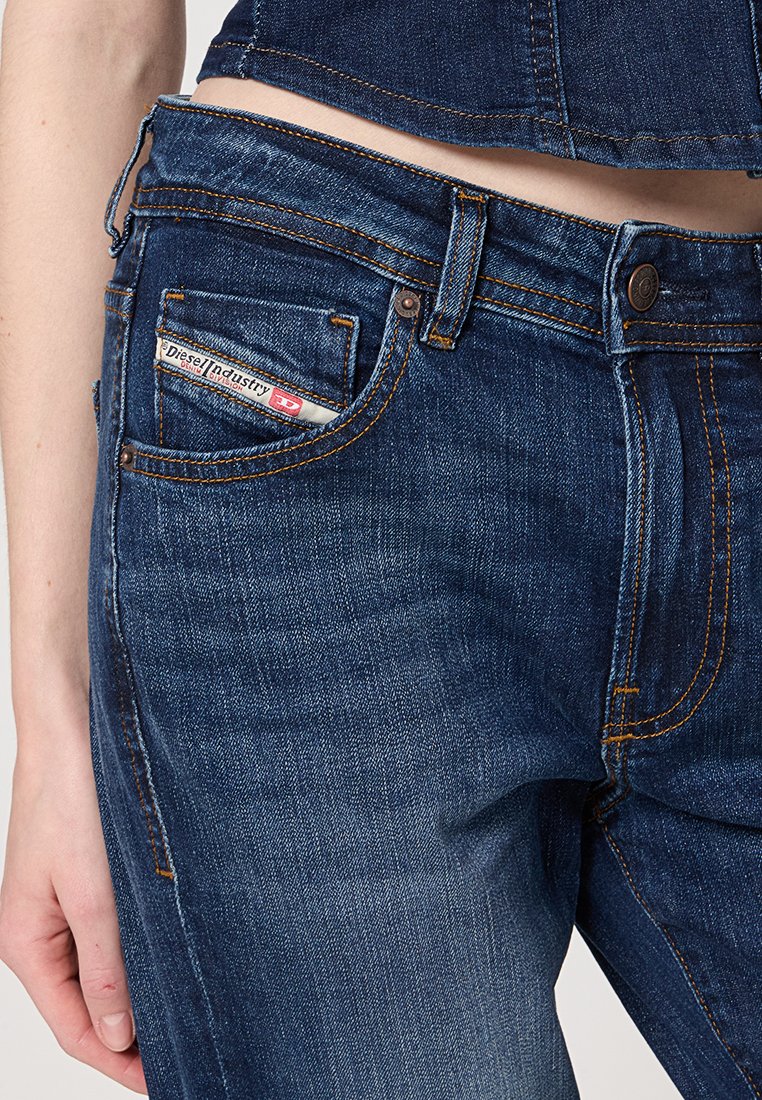 I jeans in denim blu scuro presentano un design a vita media con cuciture arancioni, una tasca frontale con etichetta e una chiusura a bottone classica.