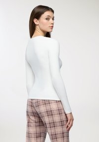 Maglietta bianca a maniche lunghe con un design aderente, abbinata a pantaloni a quadri rosa caratterizzati da una texture morbida e un motivo a quadri scuri.