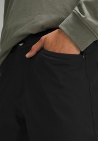 Must musta kangast püksid sirge lõikega, küljetasku detail ja nupukinnitus vöökoha juures. Ülemine serv näitab beeži varrukat.