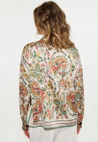 Blůza s dlouhým rukávem, která se pyšní barevným paisley vzorem na světlém pozadí, hladkým textura a kontrastními akcenty na lemech.