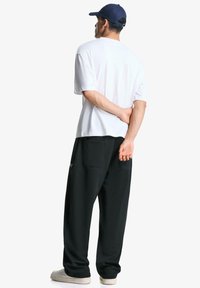 Hvid bomulds T-shirt med korte ærmer, parret med sorte teksturerede sweatpants med lommer og lyse sneakers.