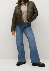 Padded olive green jacket with a high collar, paired with light blue flared jeans. Shoes are black, chunky, and textured.
