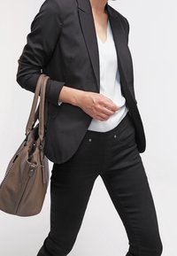 Černý tailored blejzr přes světle šedý top, v kombinaci s tmavými džíny. Hnědá texturovaná kabelka je přehozená přes rameno.