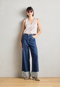 Top din bumbac cu carouri, ajustat, în nuanțe de gri deschis și roz, asortat cu blugi evazați de culoare albastră, cu mansete gri desfăcute și tocuri argintii ascuțite.
