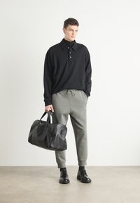 Črna polo majica s gumbi, sivi trenirki in črna usnjena športna torba. Model nosi črne vezalne čevlje. Minimalističen dizajn.