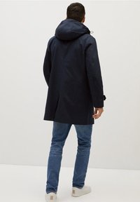 Laivastonsininen vedenpitävä takki hupulla, jossa on suora leikkaus ja säädettävät hihansuut. Karkea kangas ja siisti design. Yhdistetty vaaleiden farkkujen kanssa.