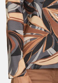 Long-sleeve top in textured fabric, featuring a multicolor floral pattern with shades of brown, gray, and cream. Visible hem and stitch details.