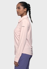 Helles rosa Hemd mit langen Ärmeln und Kragen, mit einer glatten Textur und einem Logo auf dem linken Ärmel. Kombiniert mit lila Hosen.