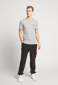 Camiseta gris de manga corta con un gráfico triangular en el pecho izquierdo, combinada con pantalones jogger negros y zapatillas blancas.
