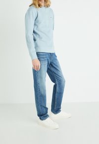 Sudadera de algodón azul claro con puños acanalados, combinada con jeans de mezclilla azul claro. El modelo lleva zapatillas blancas. Diseño simple y moderno.