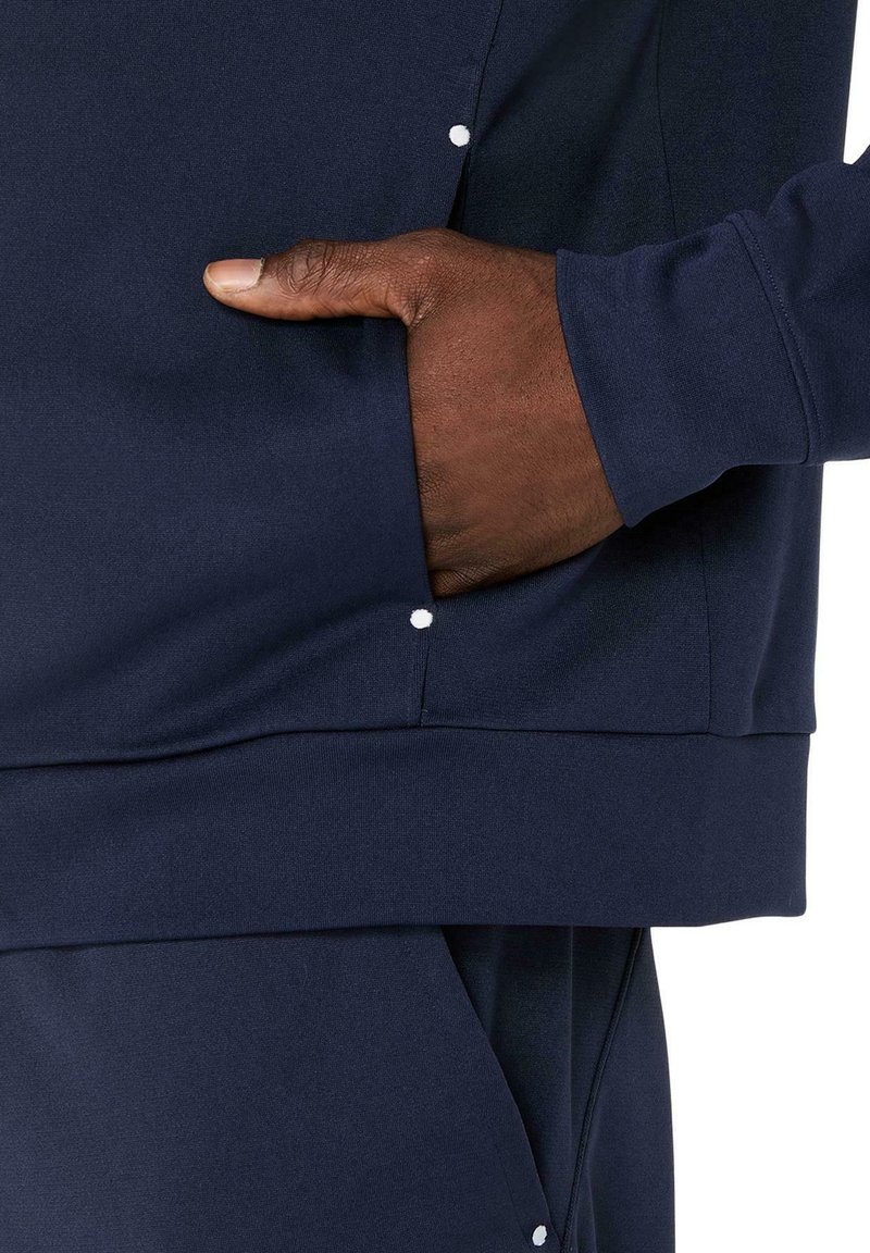 Felpa sportiva blu navy con maniche lunghe, dotata di tasca laterale e dettagli bianchi a bottoni sul bordo per un ulteriore interesse visivo.