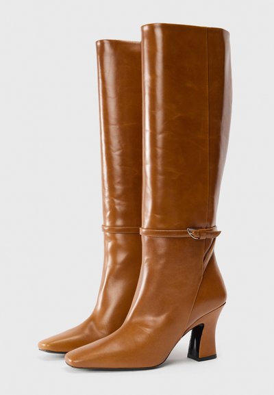 Botas de cuero de color marrón claro, hasta la rodilla, con punteras puntiagudas, un tacón alto afilado y una correa decorativa con un detalle de hebilla. Textura lisa, diseño minimalista.