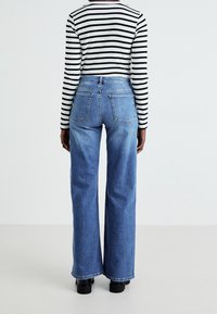 Wide-leg blue denim jeans with contrasting stitching, pockets at the back, and a high waist, paired with a black and white striped long-sleeve shirt.