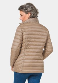 Giacca puffer beige con motivo a righe verticali, collo alto e chiusura con zip. Texture morbida e silhouette aderente, ideale per il layering.