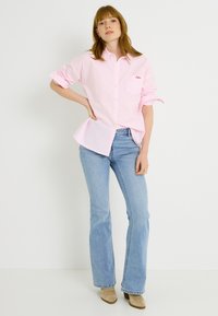 Camisa rosa claro a rayas con botones y un bolsillo, combinada con jeans azul claro acampanados y botines beige.