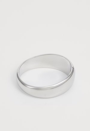 Pulseira de metal prateado com um design liso e arredondado e um brilho subtil; apresenta uma ligeira abertura para um fácil uso.