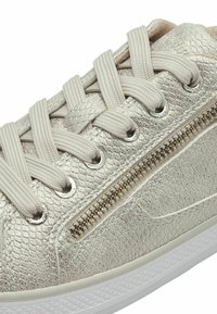 Sneaker metallico argento con una finitura texture, dotato di lacci beige piatti, occhielli argento e dettaglio con cerniera laterale. Suola in gomma bianca.