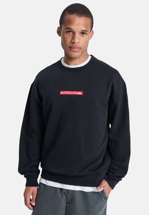 Sudadera negra con cuello redondo, con un logotipo bordado en rojo de "QUIKSILVER" en el centro. El material parece suave y tiene un corte relajado.