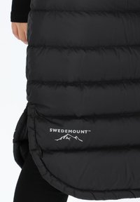 Black puffer vest with horizontal stitching, featuring a rounded hem and Swedemount logo. Smooth, shiny fabric with a soft texture.