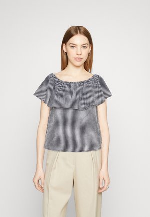 Blouse dégageant les épaules en vichy noir et blanc avec une première couche volantée, des manches courtes et une coupe décontractée. Le tissu est léger et texturé.