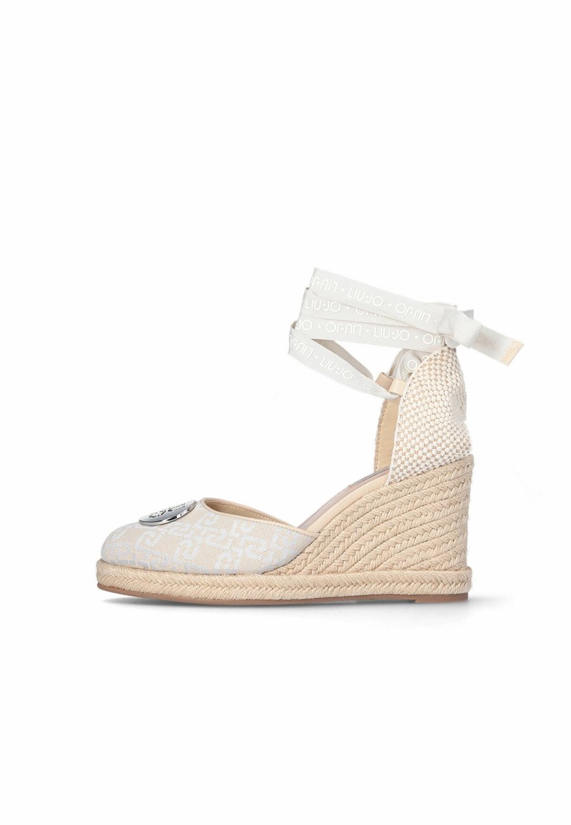 Espadrille beige à talon compensé avec dessus en tissu texturé, ornement logo sur l'avant, et lanières blanches à nouer autour de la cheville. Talon enveloppé de jute.