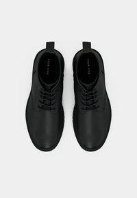 Black leather lace-up shoes with rounded toe, textured upper, padded collar, and pull tab at the rear; minimalist design.