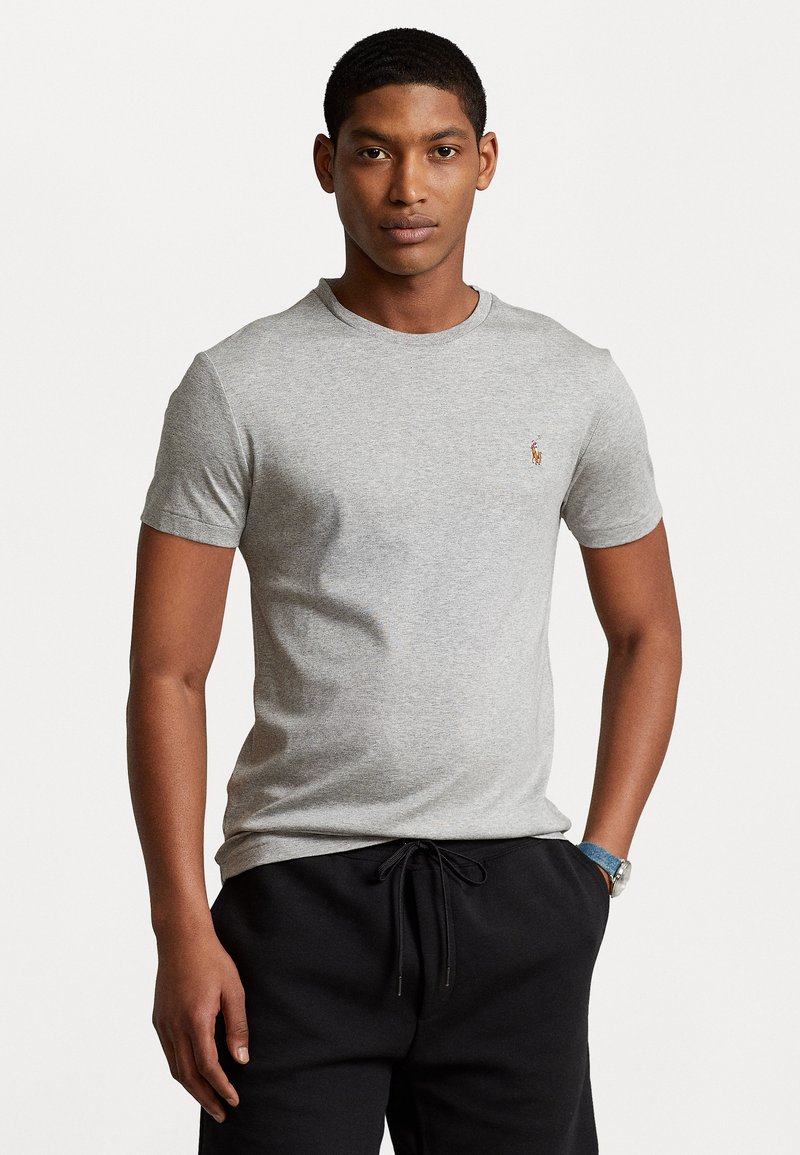 Tricou gri din bumbac, cu mâneci scurte, guler rotund și logo brodat în contrast pe piept, asociat cu pantaloni de trening negri.
