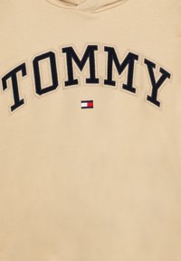 Felpa beige con la parola "TOMMY" ricamata in nero e un piccolo logo rosso, bianco e blu sul davanti. Texture morbida.
