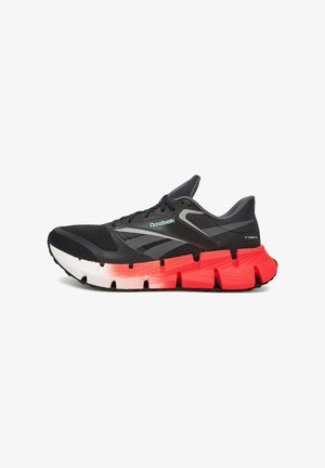 Adidași Reebok cu un superior din plasă neagră, detalii gri și o talpă intermediară din spumă groasă în gradient de la alb la roșu. Prezintă șireturi și branding.