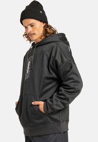 Zwarte hoodie van gladde stof met een voorzak, een capuchon met trekkoord en een contrasterend logo op de borst. Ribgebreide manchetten maken het ontwerp af.