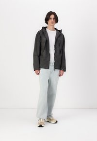 Svart jakke med hette, glidelås foran og to store lommer, kombinert med lyseblå, løse jeans og beige sneakers.
