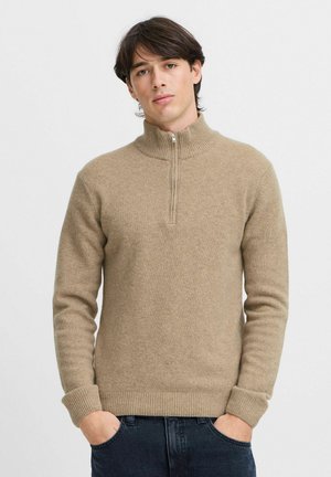 Beige knit sweater with a high collar and half-zipper. Features ribbed cuffs and hem, showcasing a smooth texture and casual design.