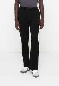 Calças de fato de treino pretas feitas de um tecido macio, com uma cintura elástica e cordão. Apresentam um corte descontraído e um design de perna reta.