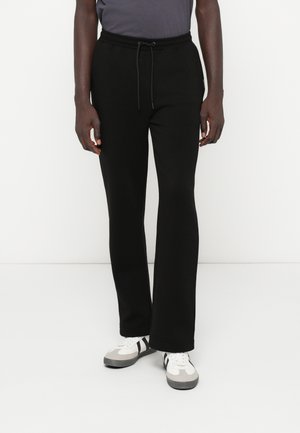 Czarne dresy wykonane z miękkiego materiału z elastycznym pasem i sznurkiem. Charakteryzują się luźnym krojem i prostymi nogawkami.