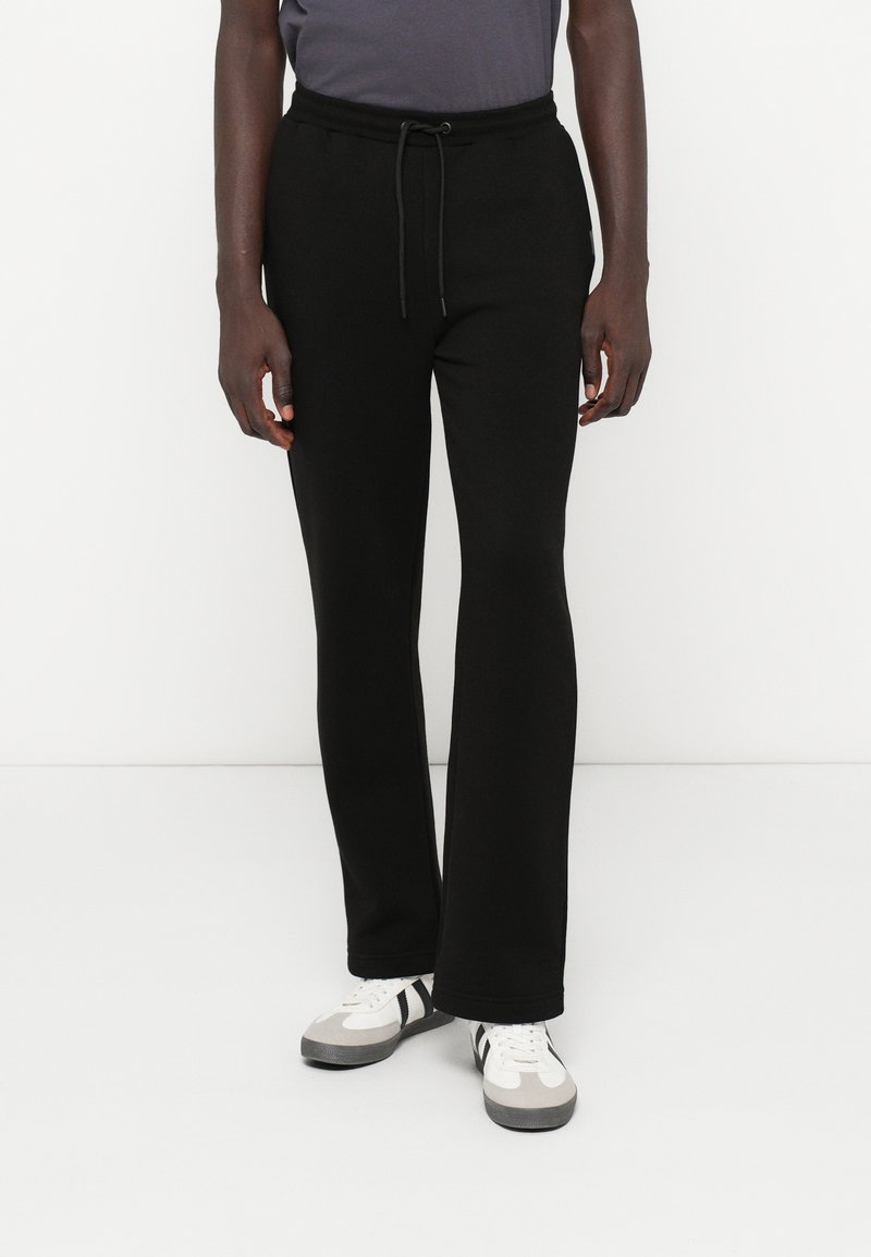 Calças de fato de treino pretas feitas de um tecido macio, com uma cintura elástica e cordão. Apresentam um corte descontraído e um design de perna reta.