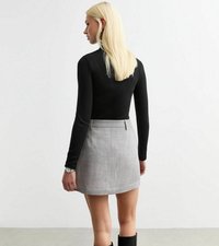Svart långärmad topp kombinerad med en grå minikjol. Kjolen har ett texturerat mönster och ett midjeband med metallaccent.