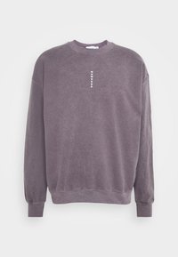 Felpa viola con scollo a girocollo realizzata in materiale morbido, con collo e polsini a coste, con la parola "NOWHERE" stampata verticalmente sul davanti.