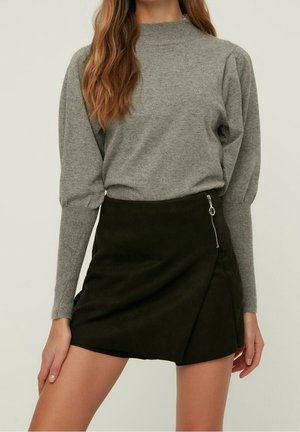 Pull en maille gris avec col montant et manches bouffantes, associé à une mini-jupe en daim synthétique vert foncé avec une fermeture éclair sur le côté.