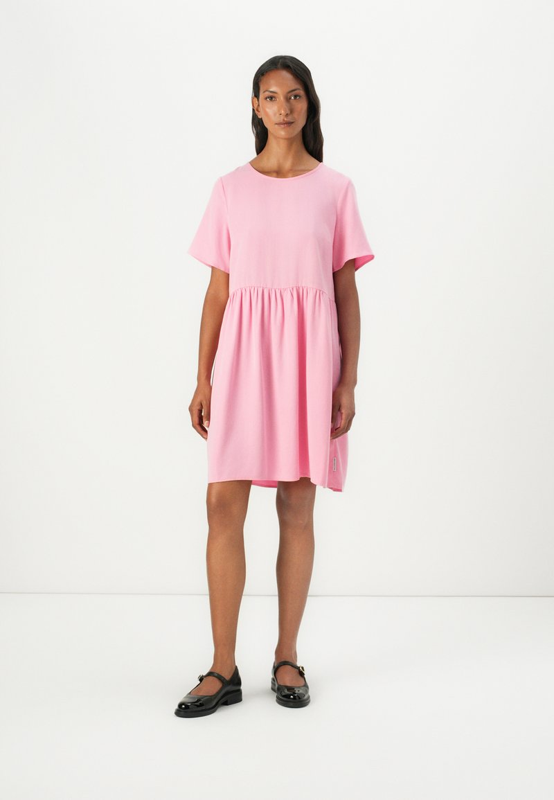 Robe rose à manches courtes avec col rond et taille froncée. Fabriquée en tissu doux, elle présente un petit logo brodé sur le côté.