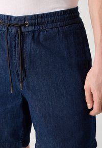 Námořnické modré kraťasy z denimu s elastickým pasem, šňůrkou na stažení a bočními kapsami. Tkanina má strukturovaný povrch.