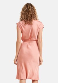 Rotes Satin-Kleid mit kurzen, aufgerollten Ärmeln, tailliertem Gürtel und knielangem Saum. Glatte Textur und minimale Designmerkmale.