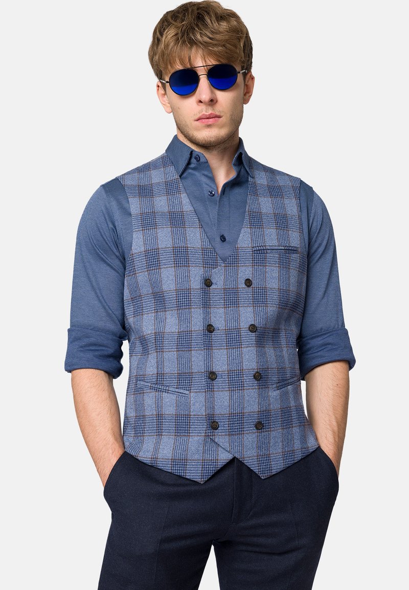 Niebieska kamizelka w wzór kratek, zestawiona z jednolitym niebieskim koszulą i granatowymi spodniami. Posiada podwójnie zapięte guziki oraz kieszenie.