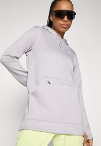 Hellblaues Kapuzensweatshirt mit einer Fronttasche und verstellbaren Kordeln, kombiniert mit leuchtend gelben Hosen. Glatte Stofftextur.