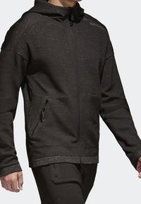 Svart zip-up jacka med en texturerad finish, som har en huva, dragkedjefickor och förstärkta sömmar för ökad hållbarhet.
