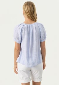 Hellblause Leinenbluse mit puffierten kurzen Ärmeln, gerafftem Ausschnitt und abgerundetem Saum; getragen mit weißen hochgekrempelten Shorts.