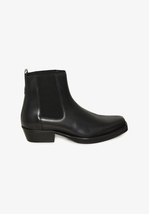 Mustast nahast pahkluu saabas elastsete külgpaneelide, madala plokktallaga ja tõmbetabaga valgel taustal.