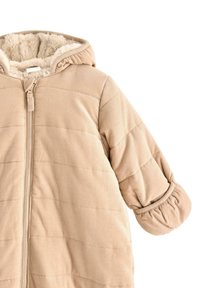Giacca puffer beige con cappuccio, texture trapuntata, tessuto a coste e polsini elasticizzati. Chiusura frontale a zip e foderata con materiale morbido e soffice.