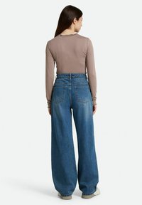 Top marrón ajustado de manga larga combinado con pantalones vaqueros de pierna ancha de cintura alta en azul. Presenta grandes bolsillos traseros y una silueta relajada.